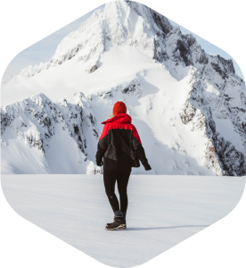 Women wearing red benie, red and black jacket and pants, standing in front of a snowy mountain.