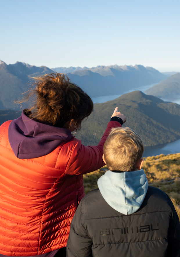 Women and child on top of a hill. The woman is pointing out to a lake.